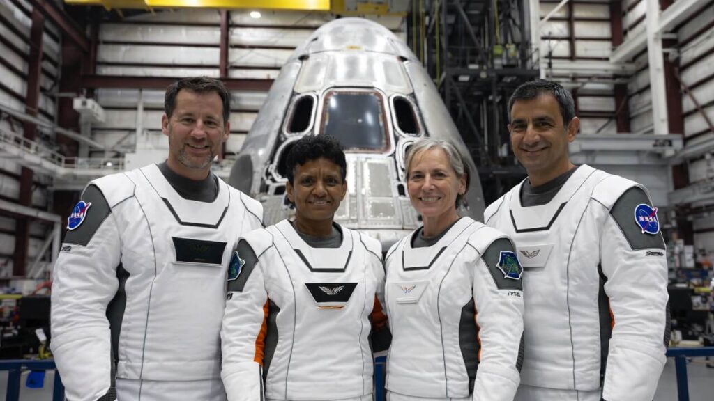 Four Artemis II astronauts in NASA spacesuits posing in front of the Orion spacecraft